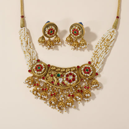 A set of traditional Indian jewelry, consisting of a choker necklace and earrings, adorned with gold, red, and green stones, and white faux pearls.