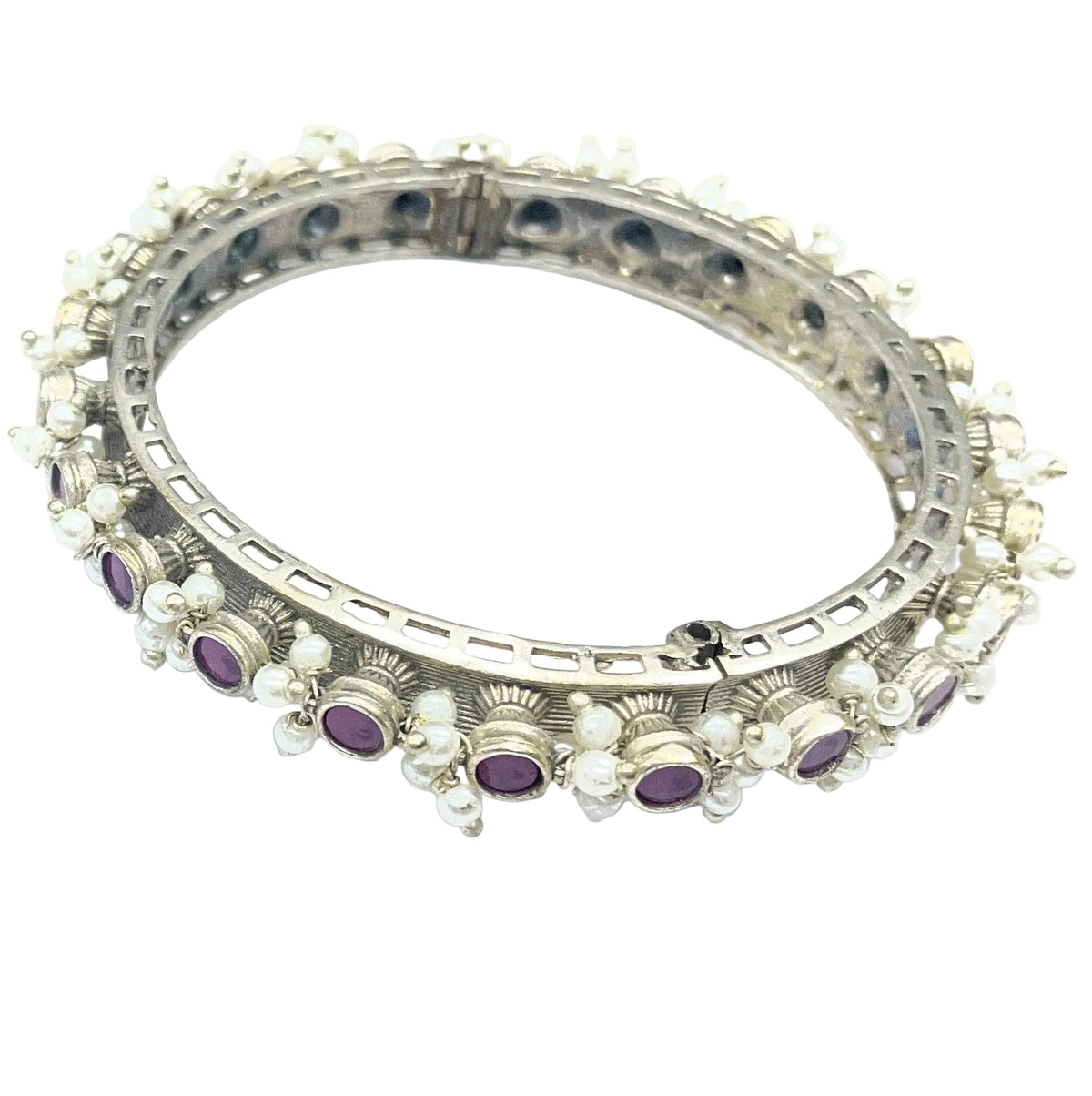 A pair of silver-toned huggie bangles decorated with rows of small clear stones and purple oval gemstones, displayed on a light blue-white background.
